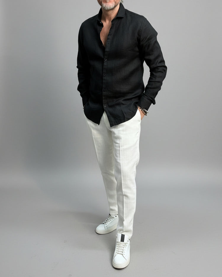 Model wearing a black linen shirt and white pants on a plain background
