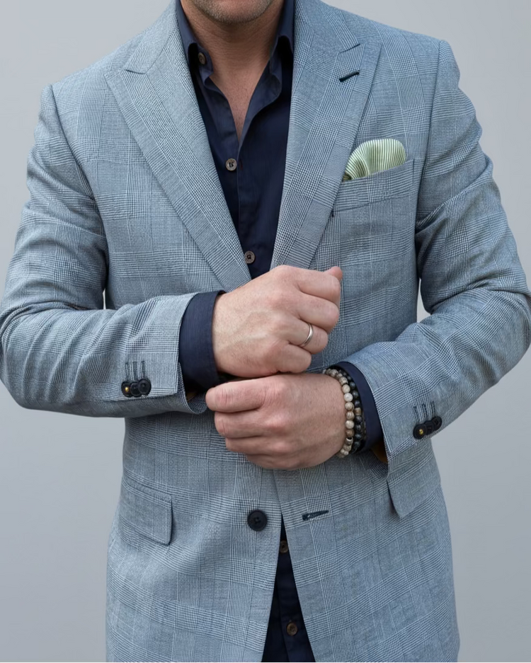 Man in a gray, blue checked suit standing in front of a light grey backdrop.