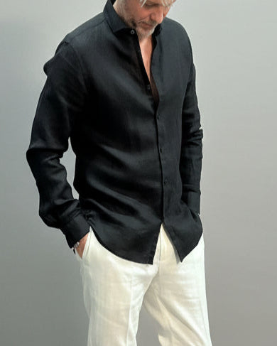 Model wearing a black linen shirt and white pants on a plain background