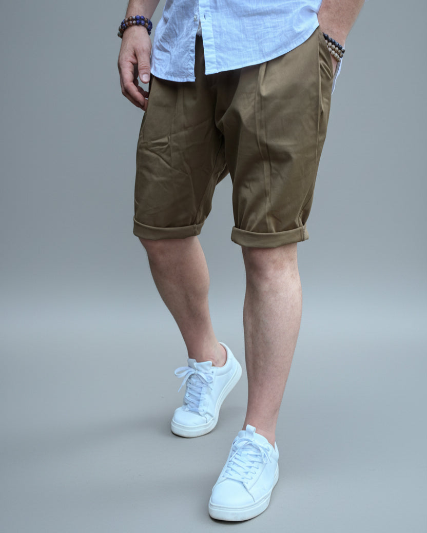 Person wearing a white shirt, brown shorts, and white sneakers in front of light grey backdrop.
