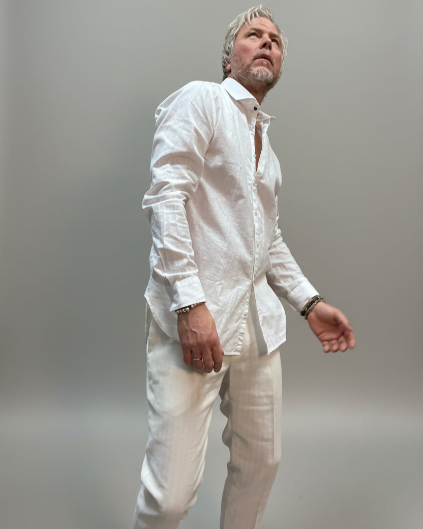 Model wearing a white linen shirt and white pants in front of light grey backdrop 