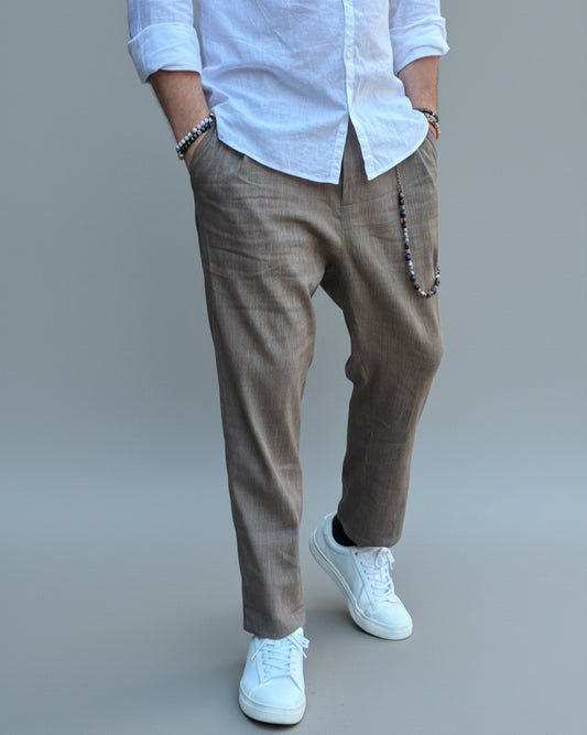 Model standing in front of light grey backdrop wearing brown linen pants and white shirt and sneakers