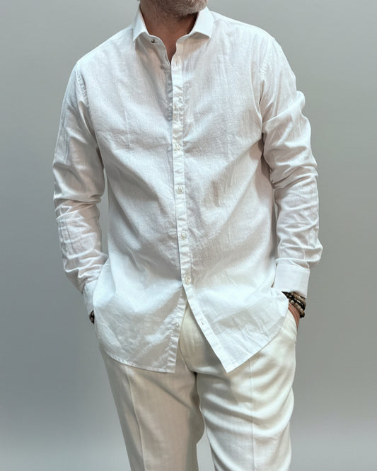 Model  wearing a white shirt and white pants in front of light grey backdrop