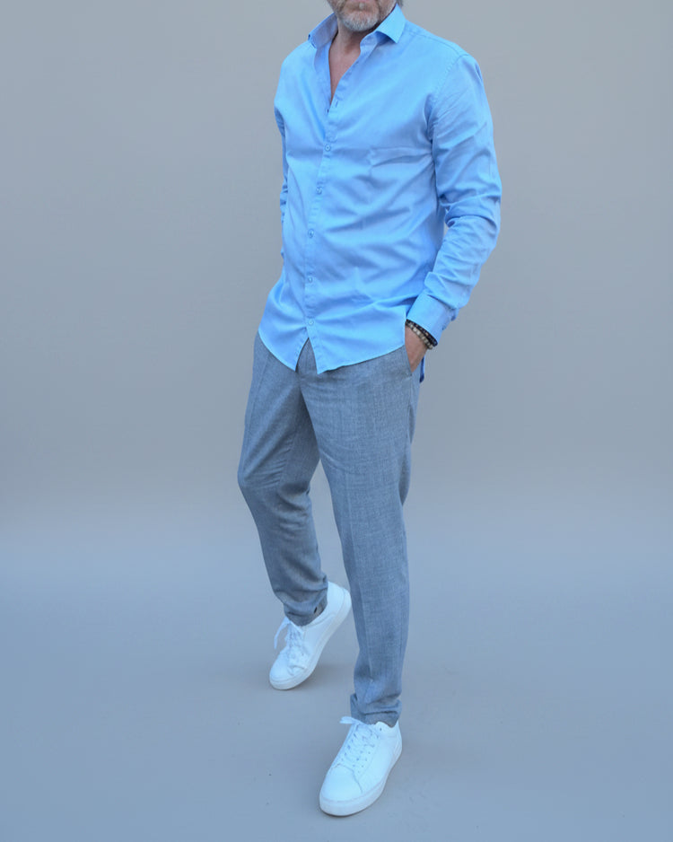 Man in a gray, blue checked pants and light blue shirt standing in front of a light grey backdrop.