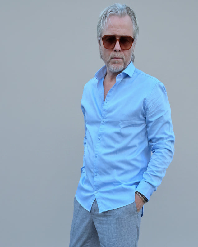Man in light blue shirt and gray pants standing in front of light grey backdrop