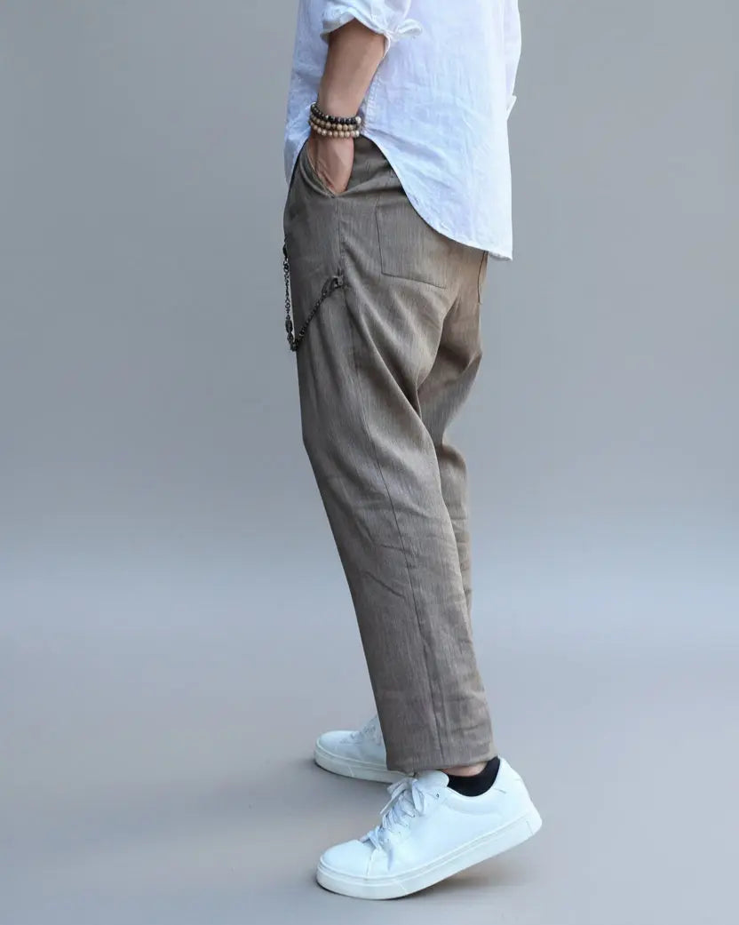 Model standing in front of light grey backdrop wearing brown linen pants and white shirt and sneakers