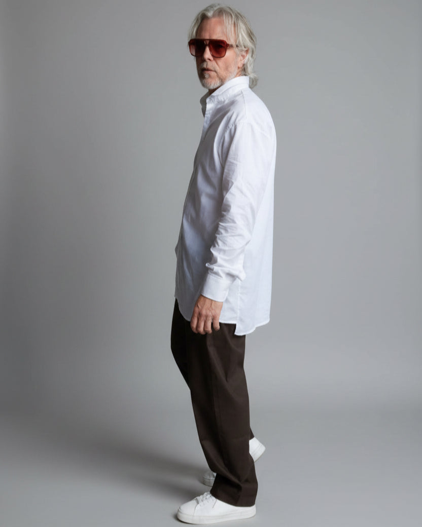 Man wearing sunglasses and a white shirt standing in front of a white brick wall.