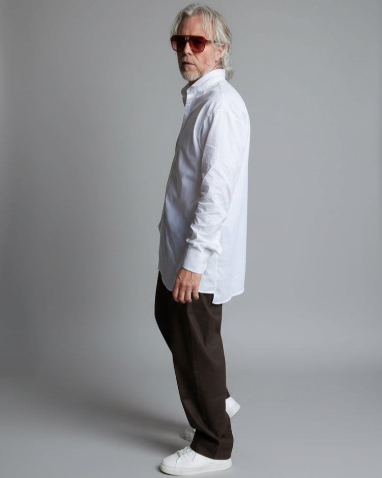 Man wearing sunglasses and a white shirt standing in front of a white brick wall.