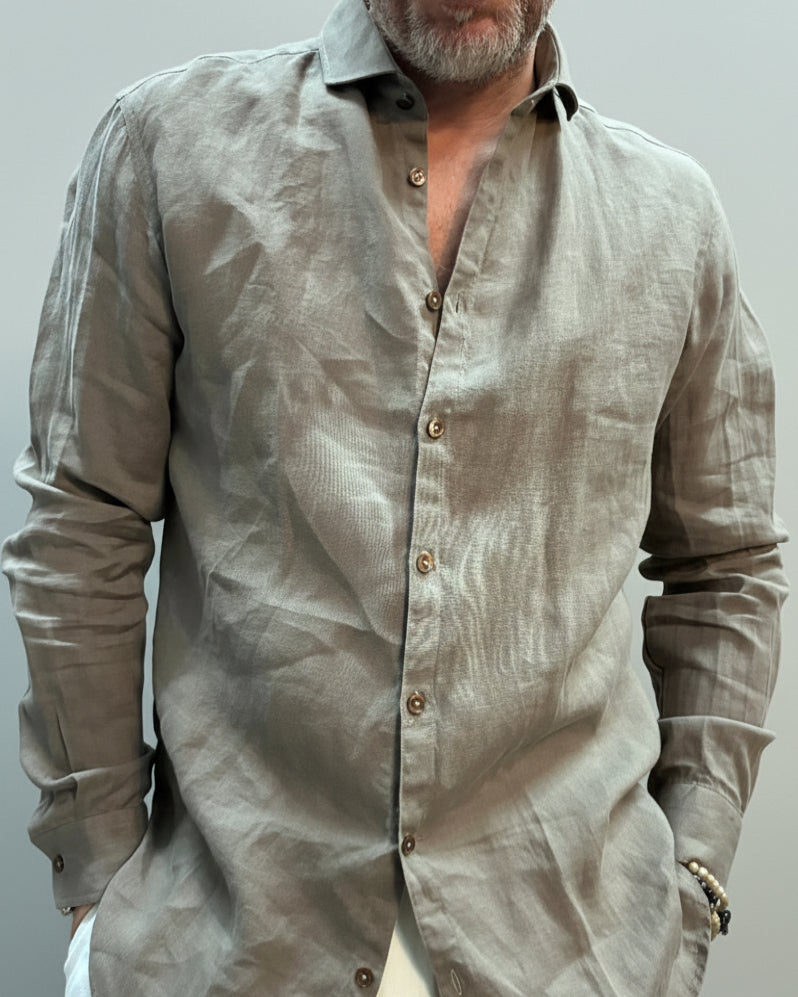 Model wearing a mud colored shirt  and white pants in front of a light grey backdrop