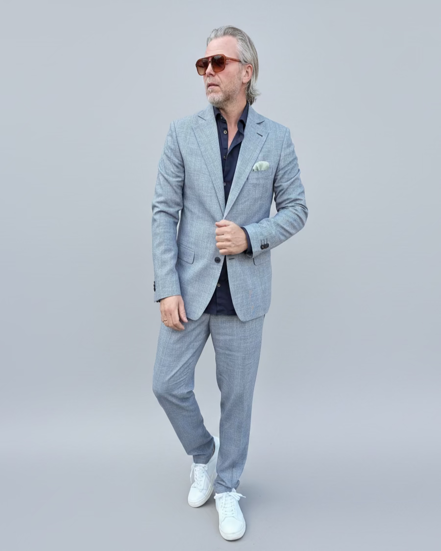 Man in a gray, blue checked suit standing in front of a light grey backdrop.
