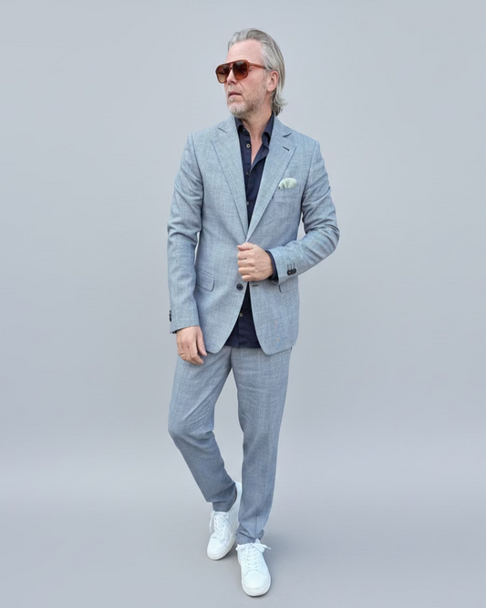 Man in a gray, blue checked suit standing in front of a light grey backdrop.