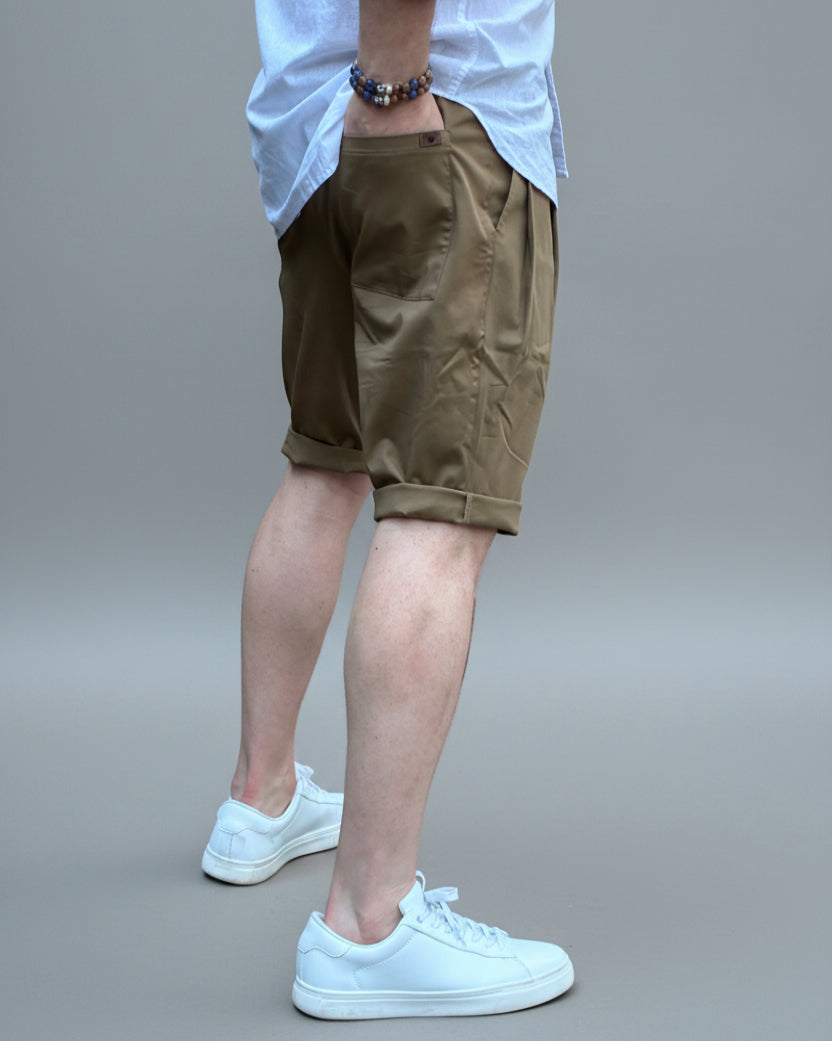 Person wearing a white shirt, brown shorts, and white sneakers in front of light grey backdrop.