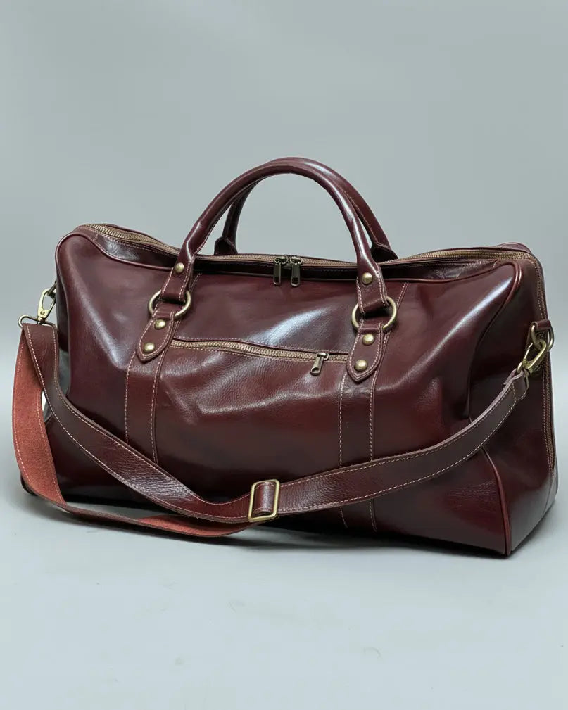 Brown leather duffel bag with shoulder strap and one puller on side pocket on a light gray fabric background