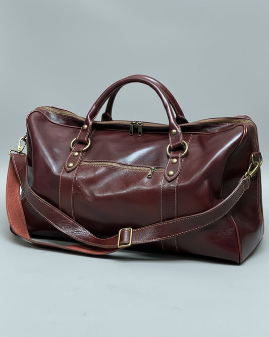 Brown leather duffel bag with shoulder strap and one puller on side pocket on a light gray fabric background