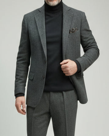 Person wearing a gray herringbone suit against a neutral background