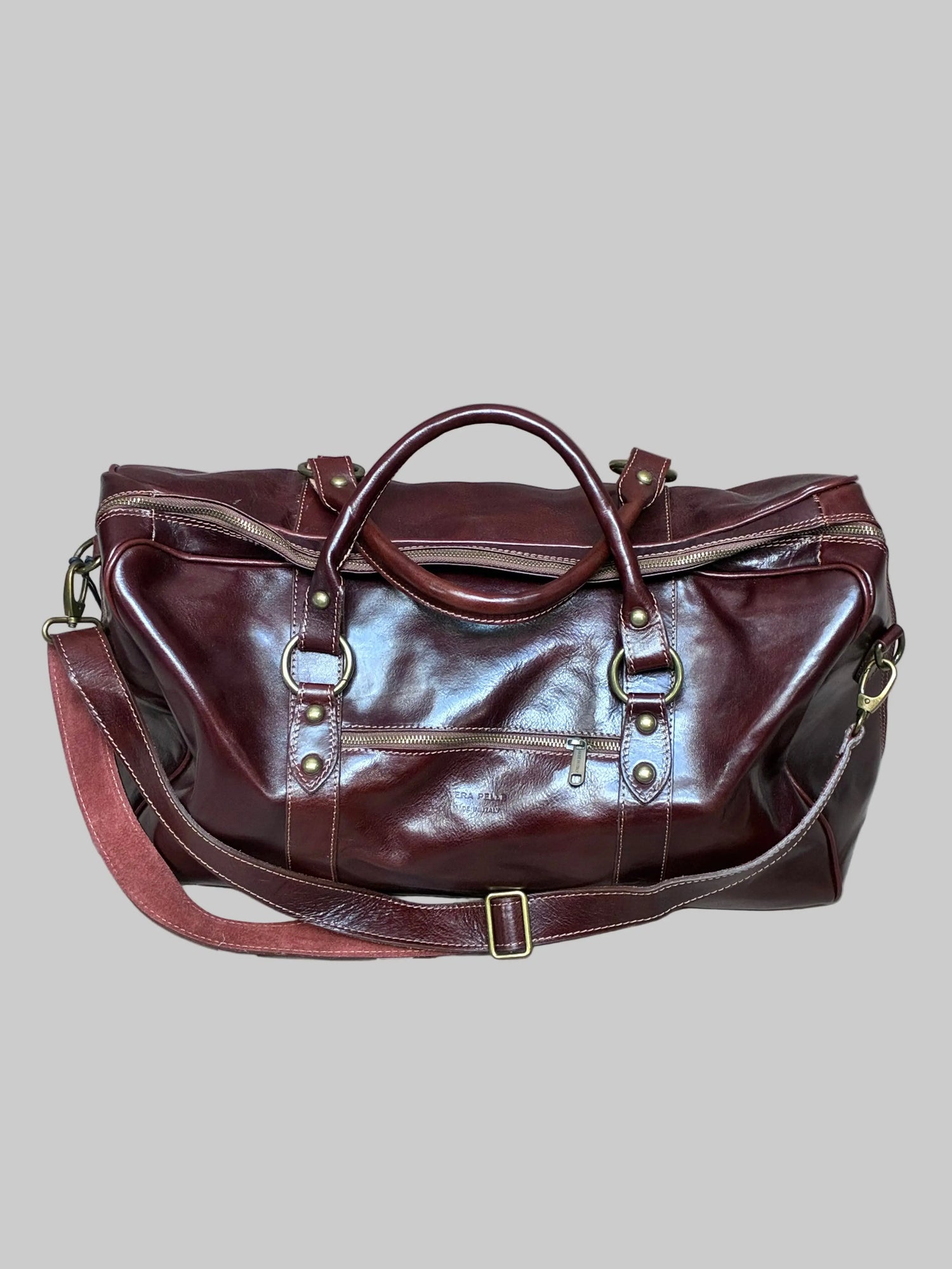 Brown leather duffel bag with shoulder strap and one puller on side pocket on a light gray fabric background