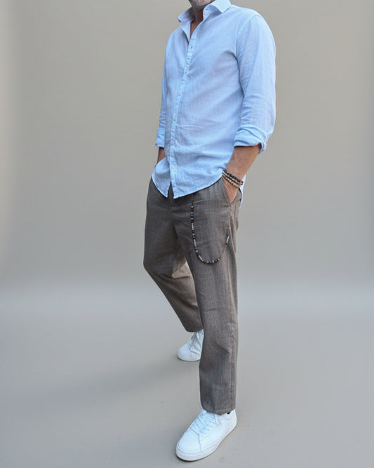 Model standing in front of light grey backdrop wearing brown linen pants and white shirt and sneakers