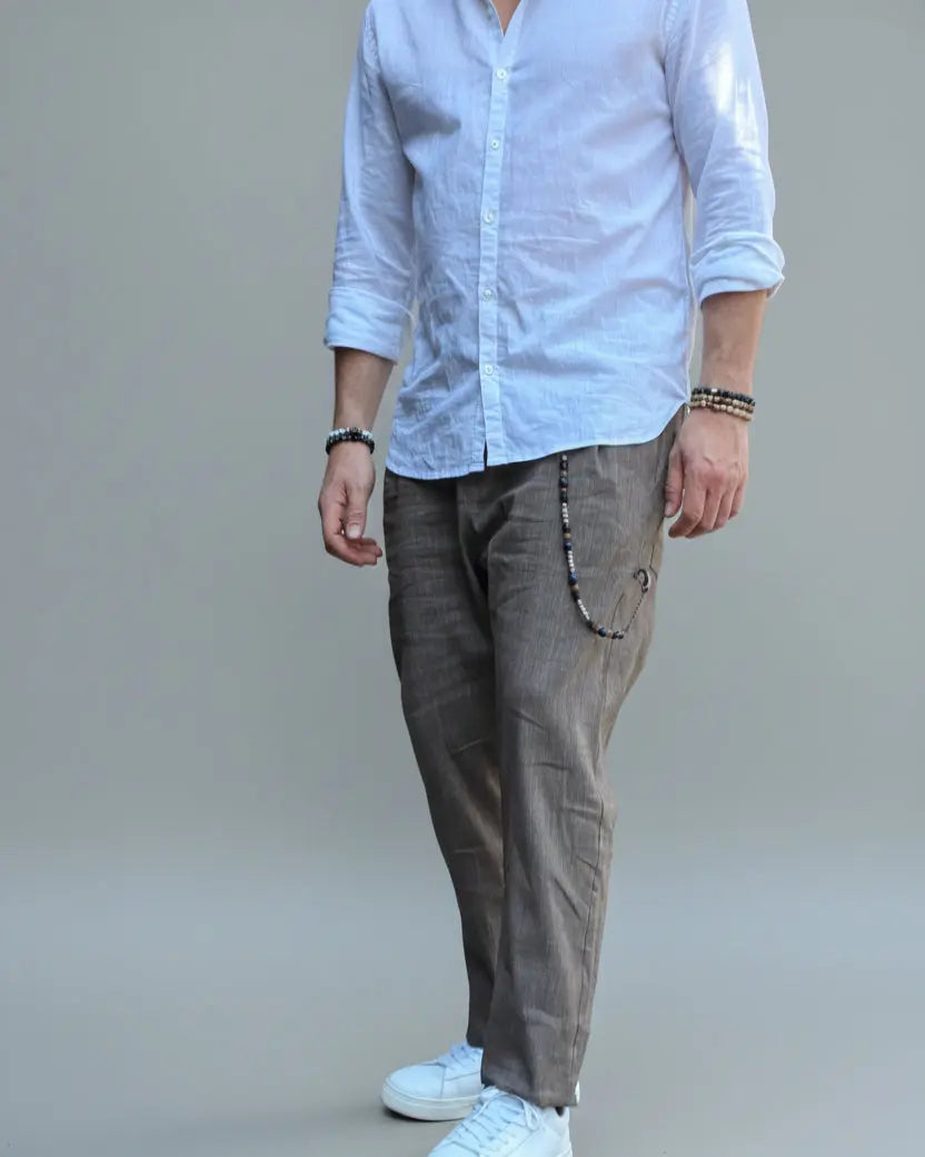 Model standing in front of light grey backdrop wearing brown linen pants and white shirt and sneakers