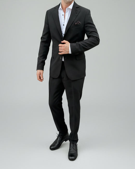 Model standing in front of light grey backdrop wearing black suit and white shirt.