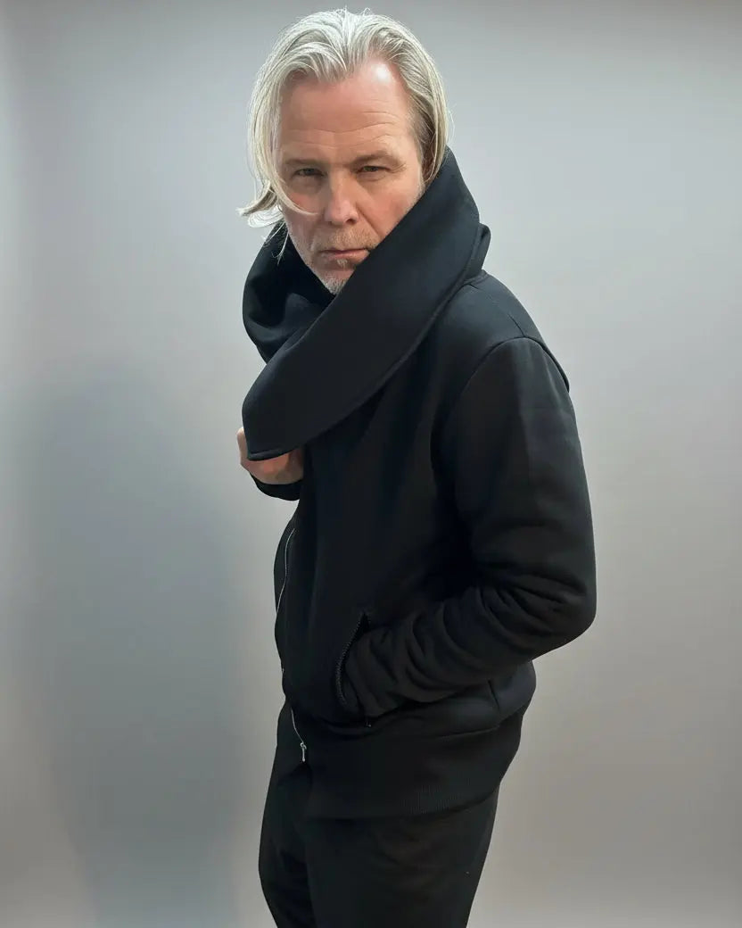 Person wearing a black hoodie on a plain background looking sharply to the camera.