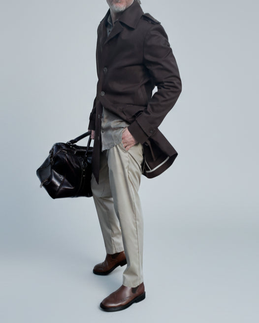 MODEL STANDING IN FRONT OF L. GREY BACKDROP WEARING A BROWN TRENCH COAT