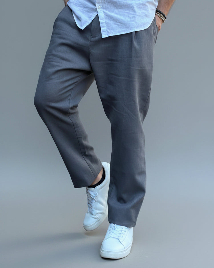 Person wearing a white shirt, gray linen pants, and white sneakers on a light grey background in a dynamic possition.