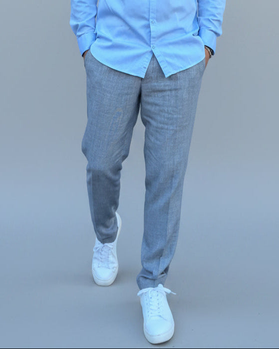 Man in a gray, blue checked pants and light blue shirt standing in front of a light grey backdrop.