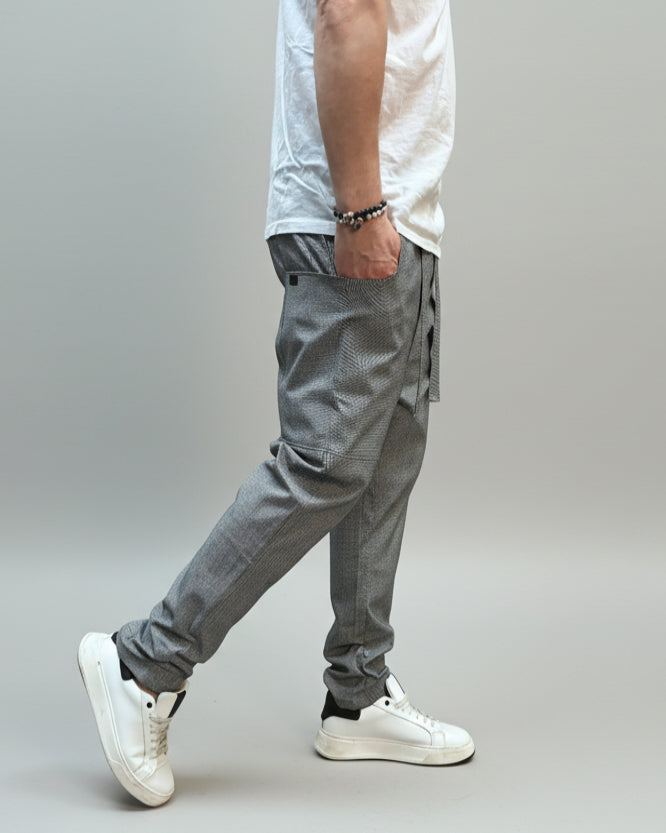 Person wearing grey dogtooth pants and white T-shirt and white sneakers on a gray floor.