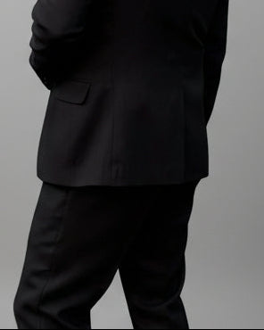 Model standing in front of light grey backdrop wearing black suit and white shirt.