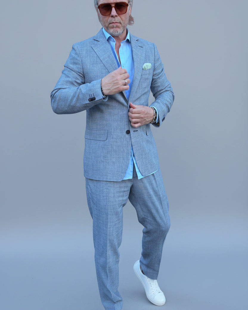 Man in a gray, blue checked suit standing in front of a light grey backdrop.