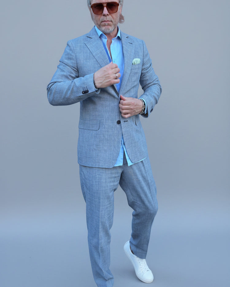 Man in a gray, blue checked suit standing in front of a light grey backdrop.