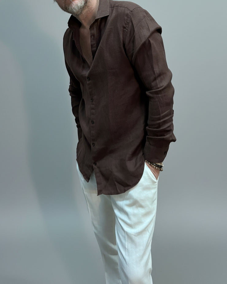 Model wearing a brown button-up shirt and white pants against light grey backdrop