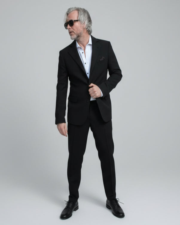 Model standing in front of light grey backdrop wearing black suit and white shirt.