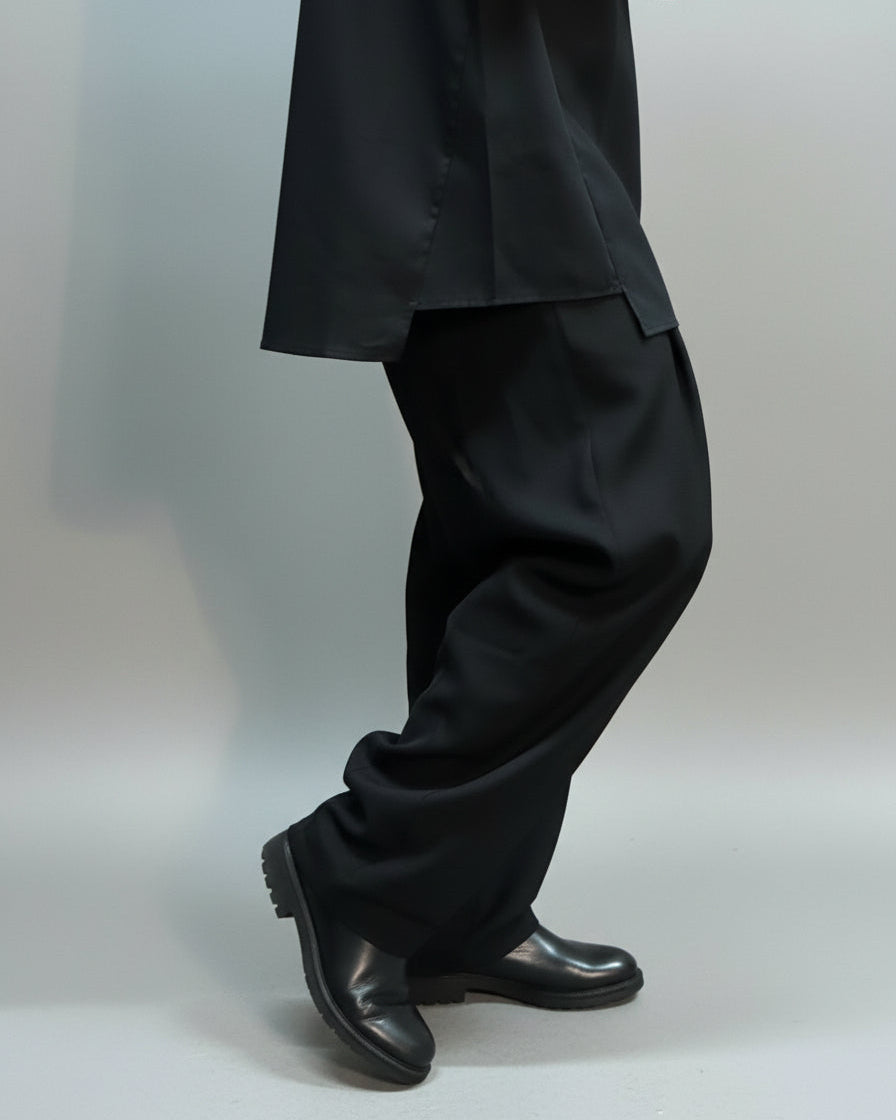 Person wearing a black suit and shoes standing on the side facing the camera showing only details