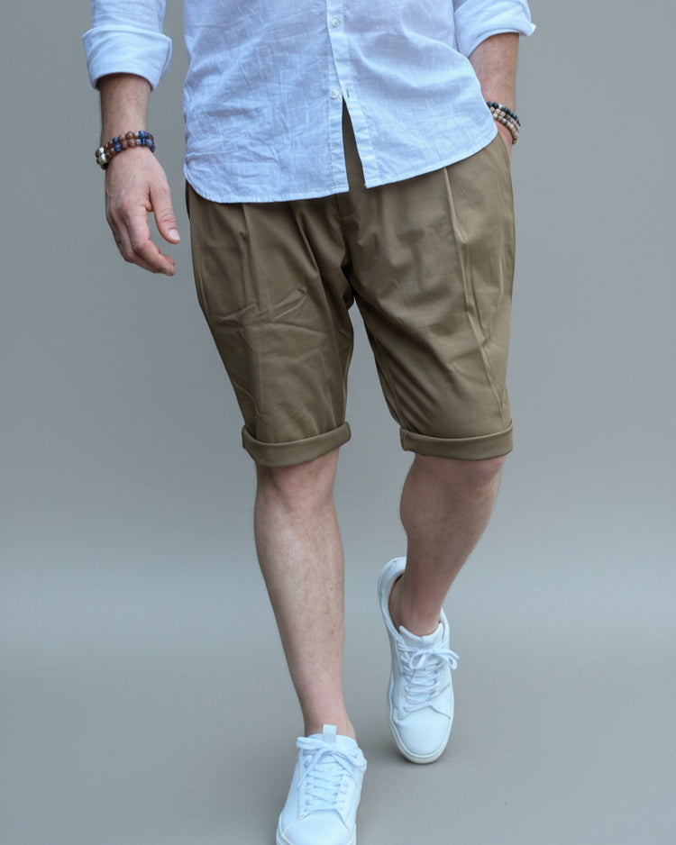 Person wearing a white shirt, brown shorts, and white sneakers in front of light grey backdrop.