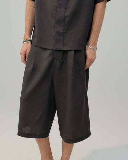 A person wearing a black black short-sleeve V-neck top and matching loose cropped pants photographed against a plain light gray studio background.