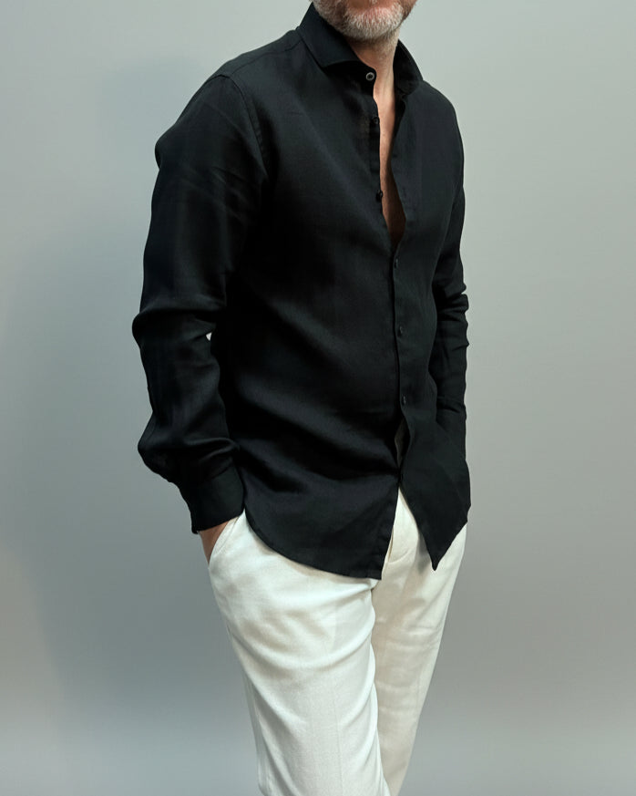 Person wearing a black linen shirt and white pants on a plain background