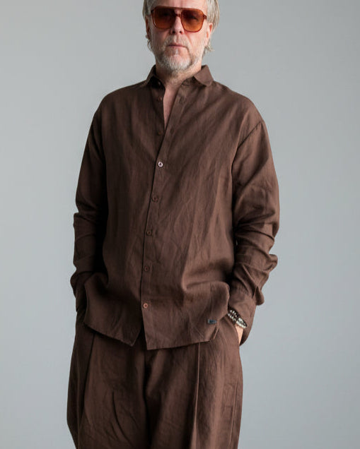 Man in a brown outfit standing against light grey backdrop