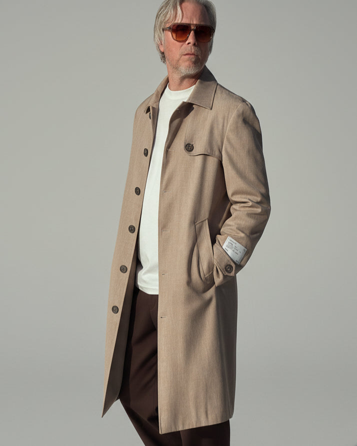 MODEL WEARING A BEIGE COAT IN FRONT OF A GREY BACKDROP