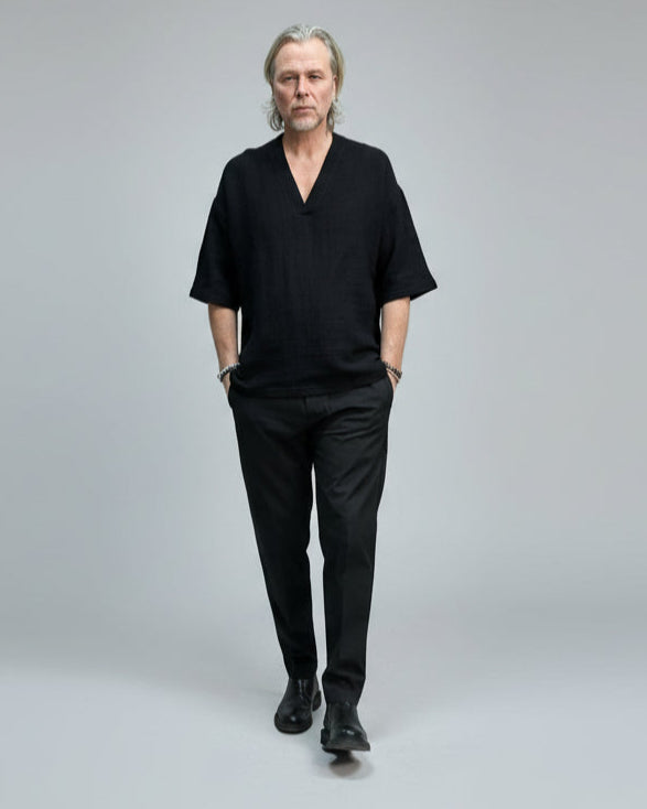 Man in black outfit standing against a light grey background