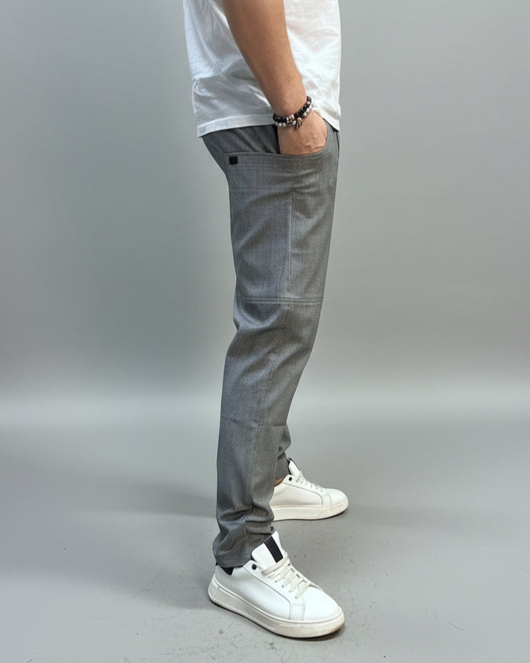 Person wearing grey dogtooth pants and white T-shirt and white sneakers on a gray floor.