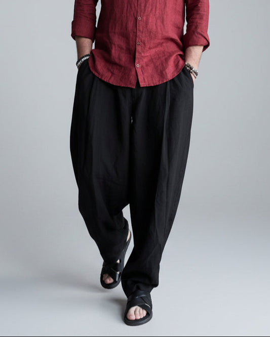 Man in a black pants and red linen shirt  standing against light grey backdrop