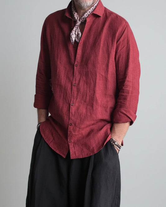Man in a black pants and red linen shirt  standing against light grey backdrop