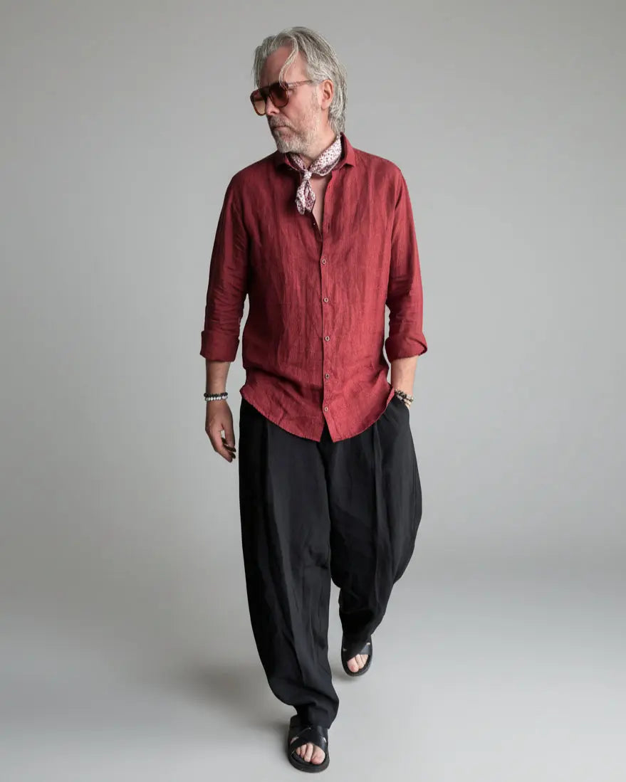Man in a black pants and red linen shirt  standing against light grey backdrop