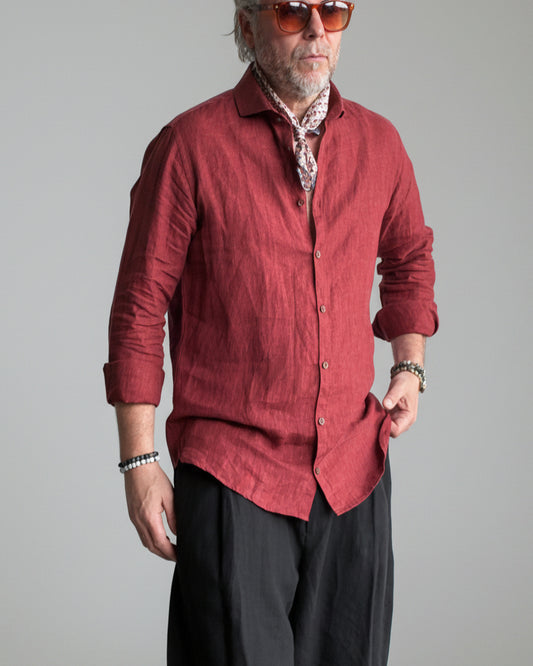 Man in a black pants and red linen shirt  standing against light grey backdrop