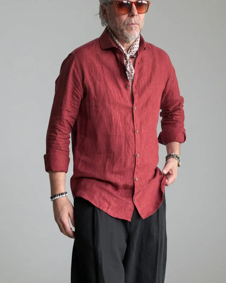 Man in a black pants and red linen shirt  standing against light grey backdrop