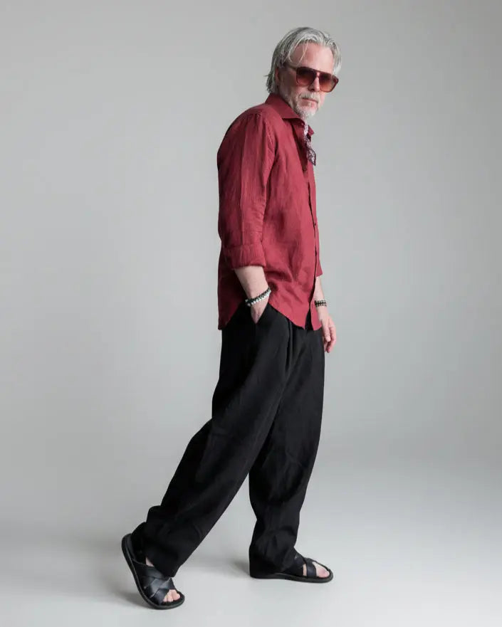 Man in a black pants and red linen shirt  standing against light grey backdrop