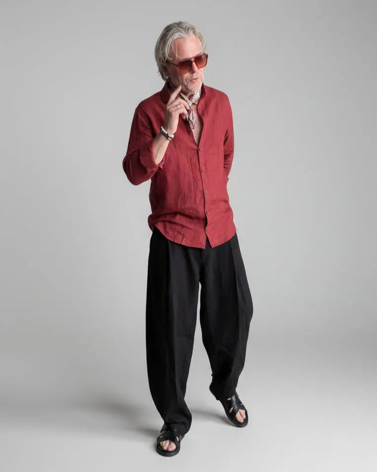 Man in a black pants and red linen shirt  standing against light grey backdrop