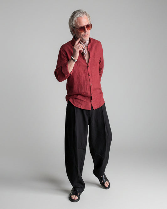 Man in a black pants and red linen shirt  standing against light grey backdrop