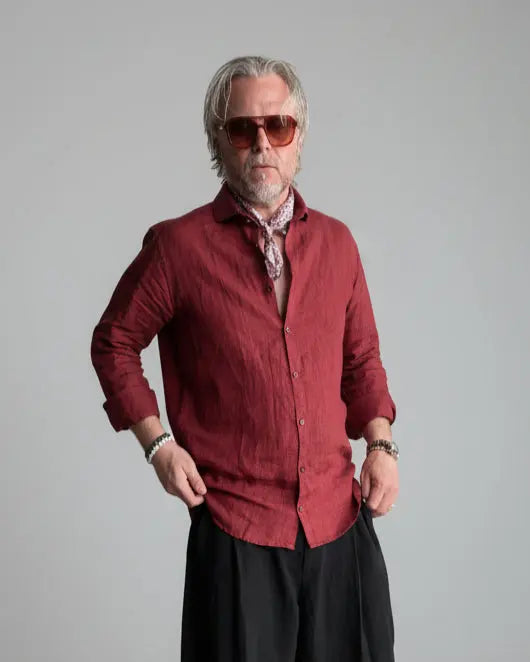 Man in a black pants and red linen shirt  standing against light grey backdrop